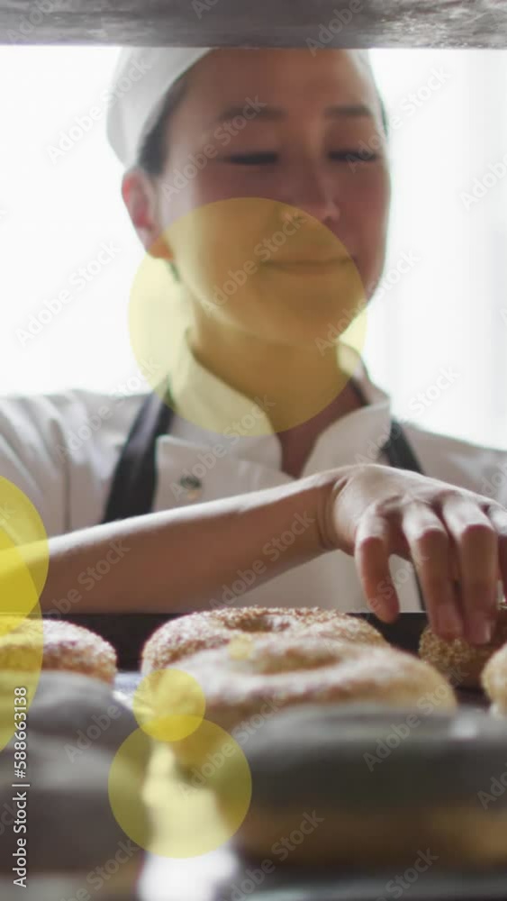 Animation of green spots over asian female baker preparing donuts Animation of green spots over asian female baker preparing donuts