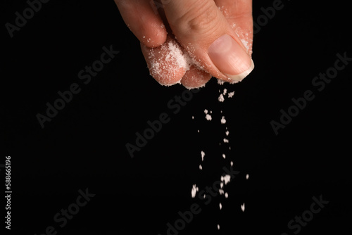 Konstfotografi Female fingers sprinkle salt on a black background, copy the space