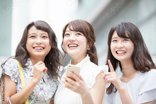 街中でスマートフォンを持ち笑う女性3人