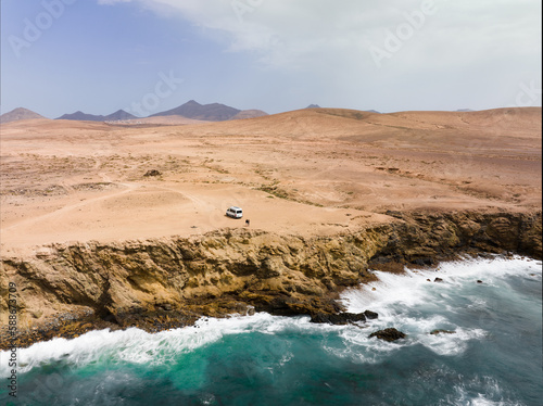 Obraz na płótnie View from above, stunning aerial view a couple with a van on a cliff bathed by the ocean. Fuerteventura, Canary Islands. Life on the road concept, nomadic lifestyle. w salonie