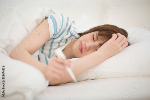 ベッドで体温計を持ち寝込む女性