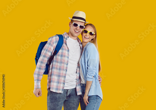 Portrait of happy young couple of female and male tourists traveling abroad on weekend. Joyful active couple of travelers in casual clothes, sunglasses and with backpack on orange background.