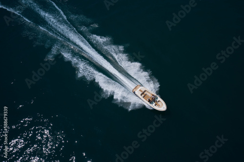 Luxury big motor boat with people fast moving on dark blue water top view. Diagonal movement of a large motor boat with people aerial view. © Berg