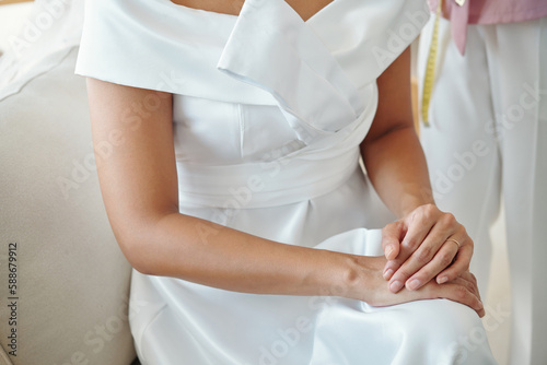 Cropped image of bride in wedding dress sitting on couch in atelier