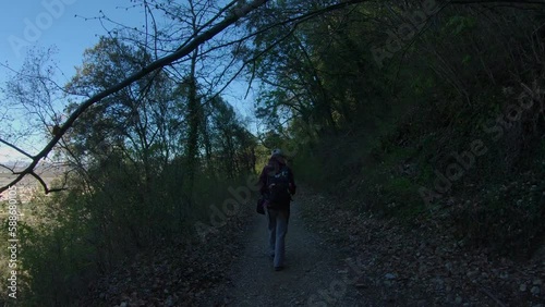 woman with backpack walking on a mountain trail in the shadow of a forest. She hike under a branch being over the path. video in slow motion