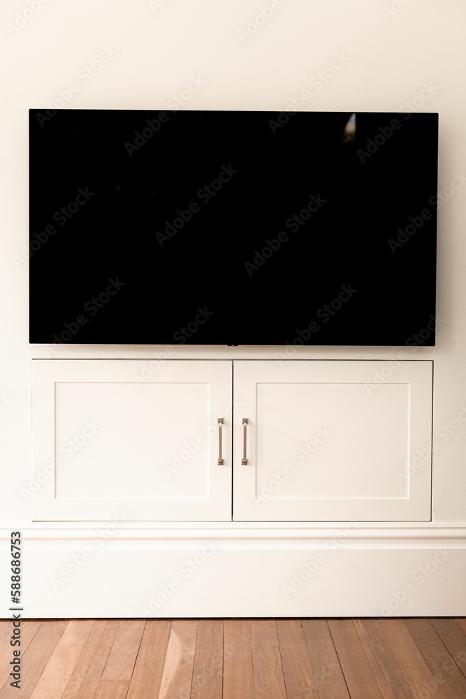 Vertical shot of a modern TV screen over a white cabinet doors on the wall