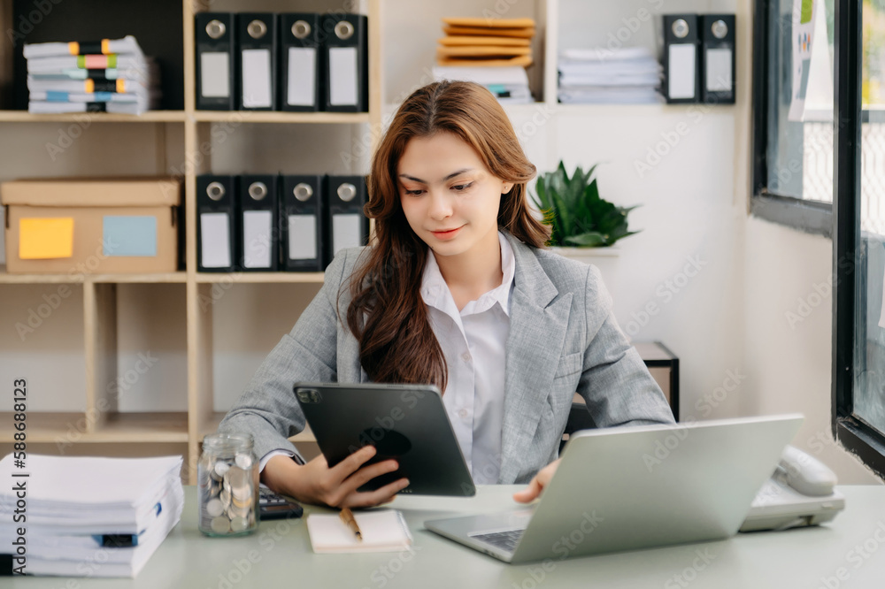Young beautiful woman using laptop and tablet while sitting at her working place. Concentrated at work. Young beautiful woman using laptop and tablet while sitting at her working place. Concentrated at work.