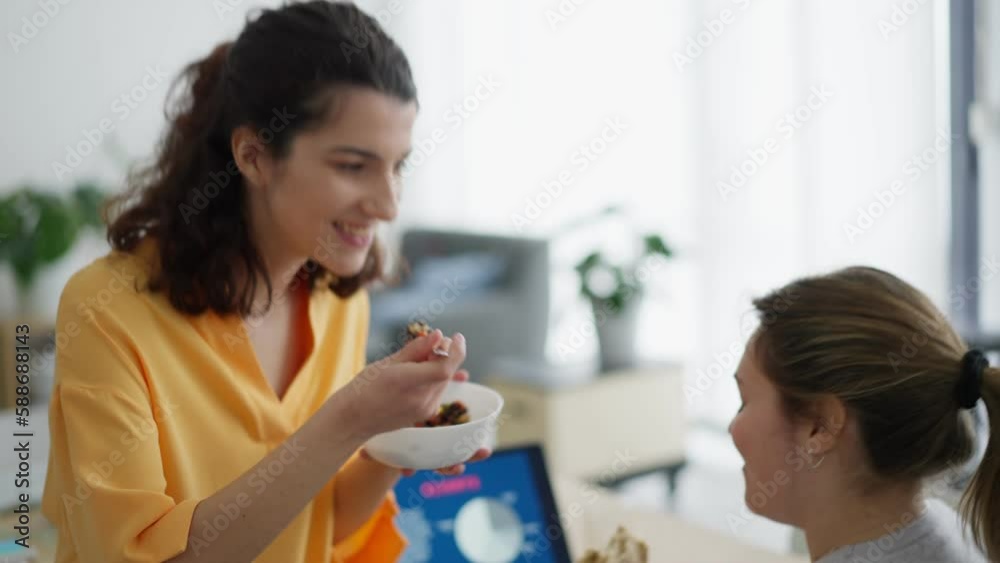 Side view of young female in casual clothes sitting at table and eating delicious food while working in office together Side view of young female in casual clothes sitting at table and eating delicious food while working in office together