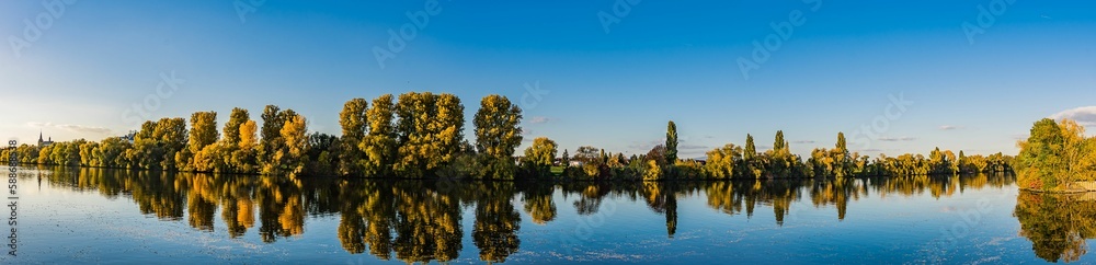 Fototapeta premium Panoramic shot of the reflection of the trees in the lake at sunset in Raunheim, Germany.