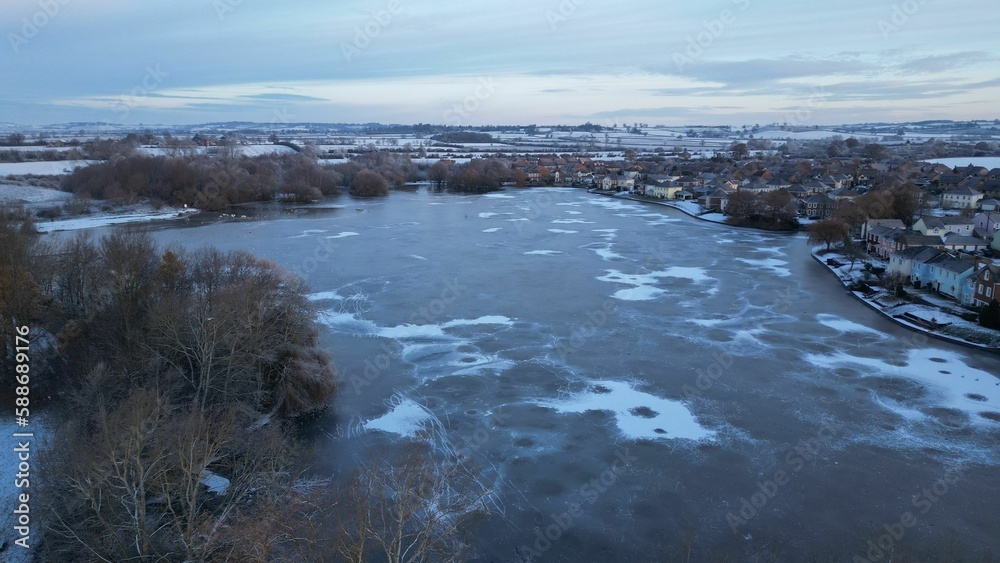 Aerial view of a frozen lake's surface, with a snowy city in the background, on a cold winter day