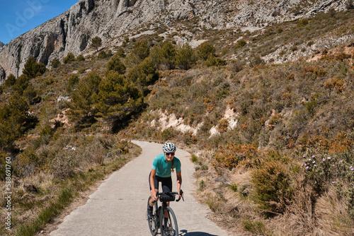 A female cyclist climbing a mountain road on a gravel bike, wearing a cycling kit and helmet.The cyclist riding between mountains, creating a beautiful and motivational image of an athlete.Spain © Ketrin