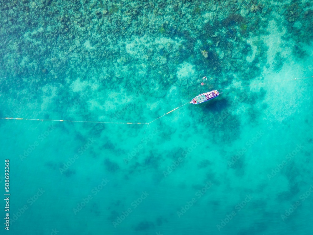 Aerial shot of the boat and snorkelers swimming in the blue waters of the sea in Thailand