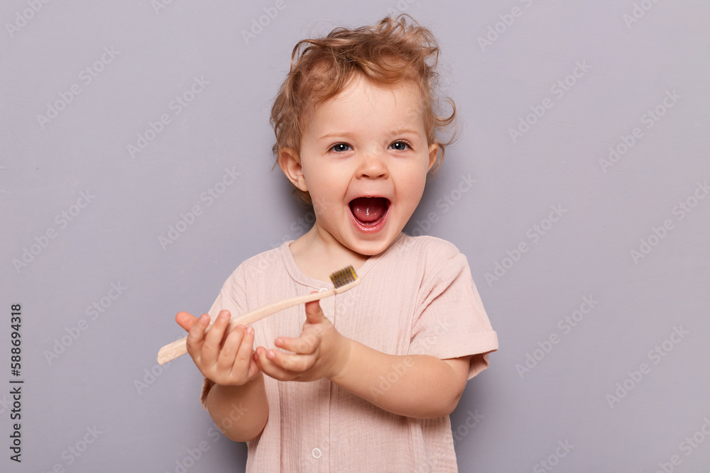 Photo of little cute child girl holding toothbrush, trying brushing teeth herself at morning every day, standing isolated on gray background. Health medical care. Photo of little cute child girl holding toothbrush, trying brushing teeth herself at morning every day, standing isolated on gray background. Health medical care.