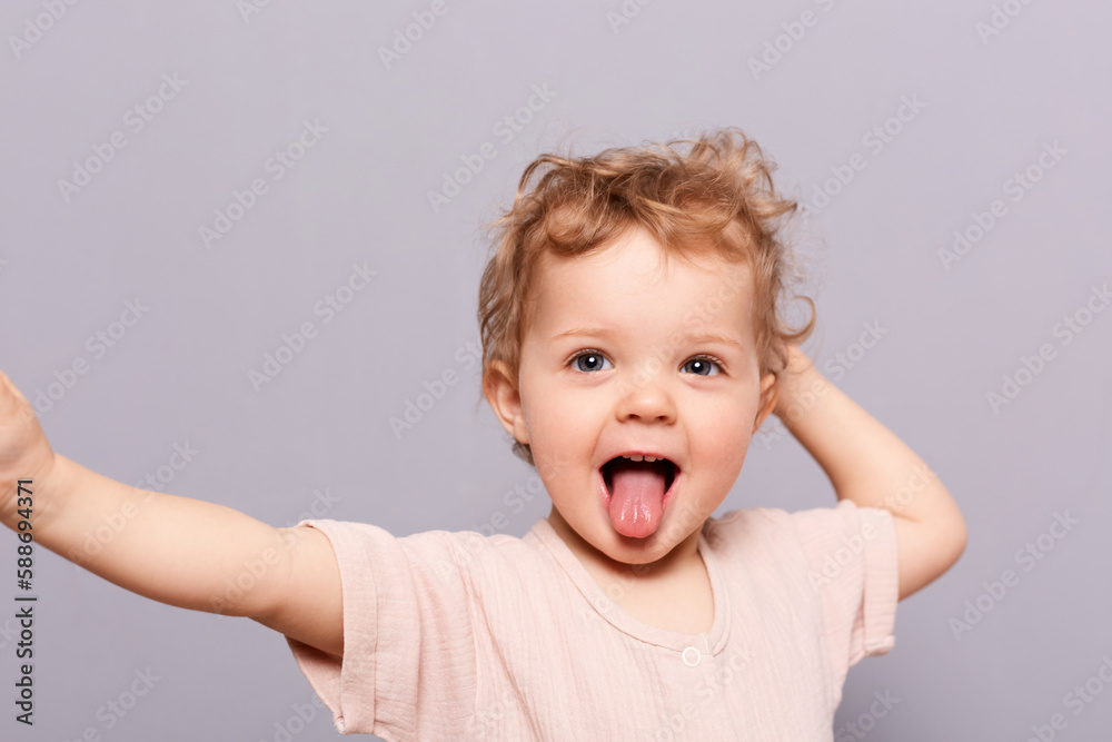 Cheerful smile child. Indoor shot of little infant girl showing tongue, standing with wide open mouth and sticking tongue out isolated over gray background. Cheerful smile child. Indoor shot of little infant girl showing tongue, standing with wide open mouth and sticking tongue out isolated over gray background.