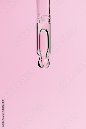 Serum in glass pipette with big bubble on light pink background. Liquid gel or essential oil with bubble macro. Trendy cosmetic product with retinol or collagen closeup. Copy space, front view.