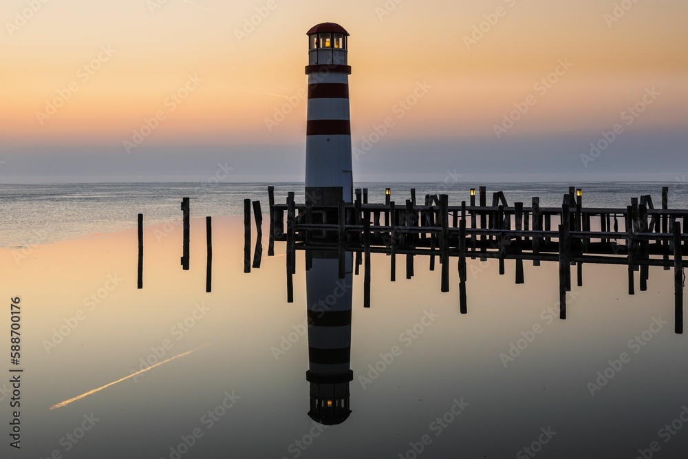 Lighthouse on pier reflecting in the water at sunset