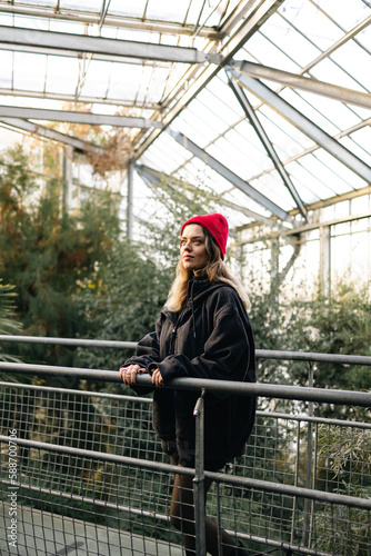 Young woman wearing red hat in botanical garden or conservatory. She explore different plant species.