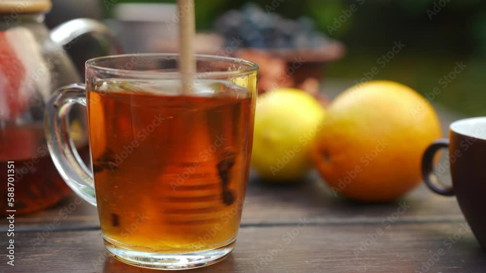 Close-up stirring honey spoon in transparent glass tea cup with tasty beverage. Female Caucasian hand mixing sweet nectar with delicious herbal hot drink on autumn day outdoors Close-up stirring honey spoon in transparent glass tea cup with tasty beverage. Female Caucasian hand mixing sweet nectar with delicious herbal hot drink on autumn day outdoors