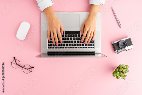 Woman’s hands working on laptop on pink table with accessories. Business background. Flat lay