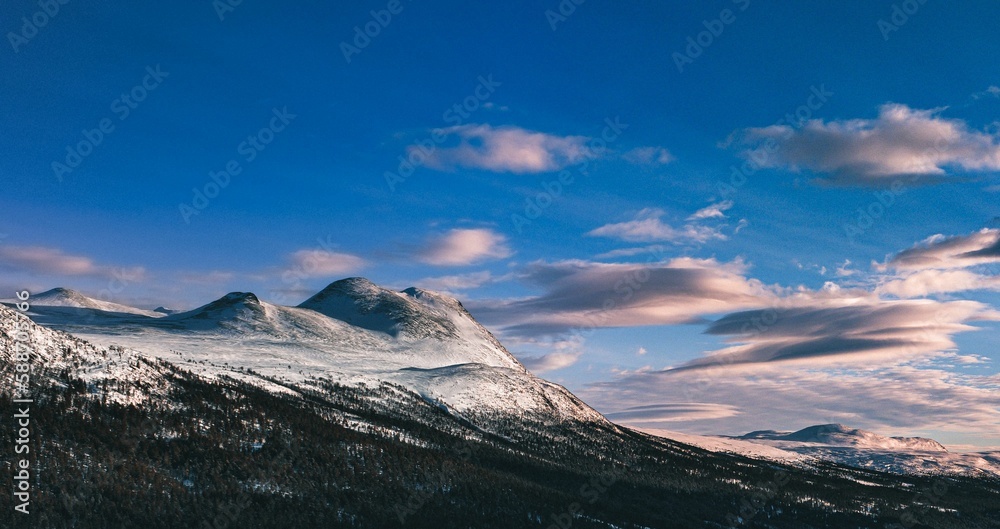 Panoramic shot of a mountain partially in snow under the blue sky and clouds