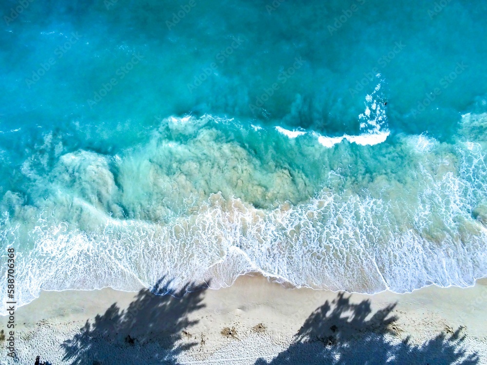 Obraz premium Aerial top view of the waves crashing on the beach with a shadow of trees in Waimanalo, Oahu, Hawaii