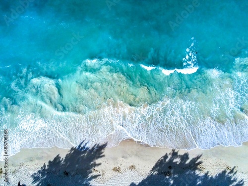 Aerial top view of the waves crashing on the beach with a shadow of trees in Waimanalo, Oahu, Hawaii photo