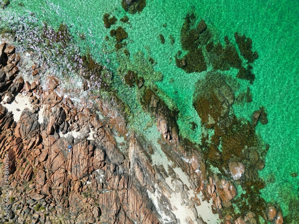 Drone view of seawater touching the stones of the coastline on a sunny day