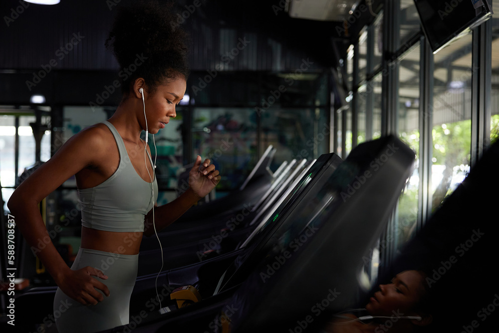 young sports woman working out with wired earbuds and running on treadmill in gym