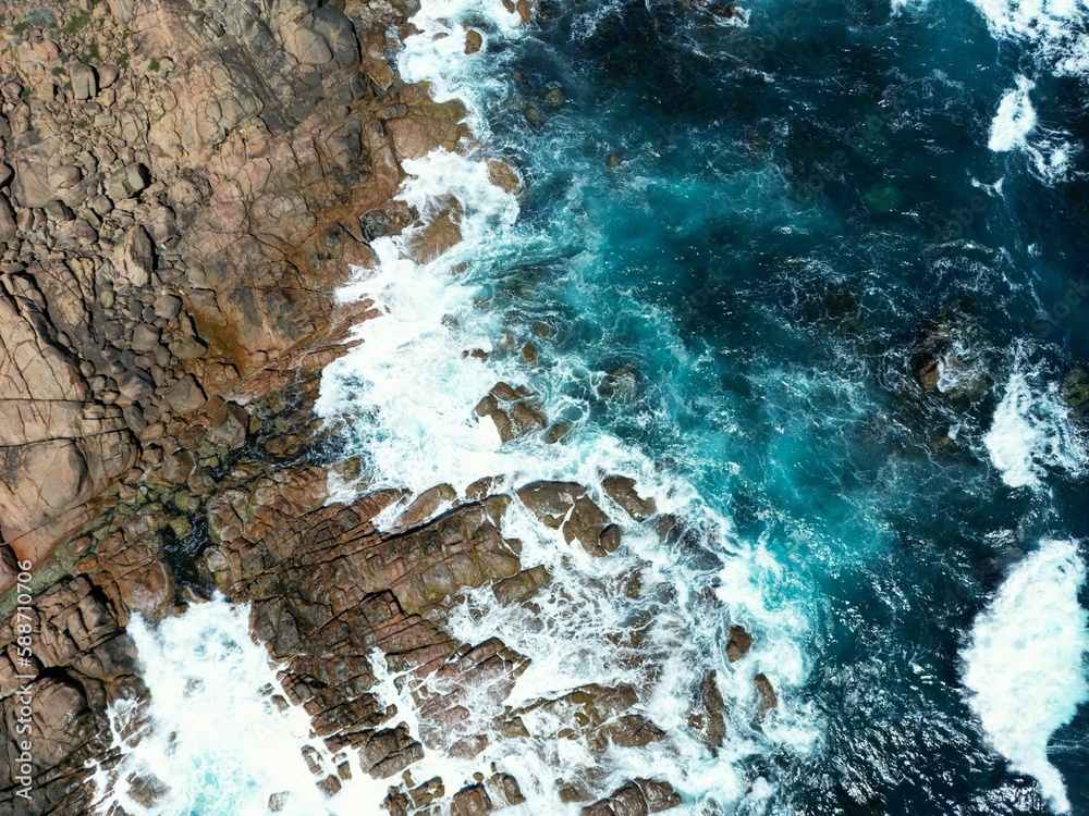 Fototapeta premium Aerial view of the coast with rocks and blue ocean waves in daylight