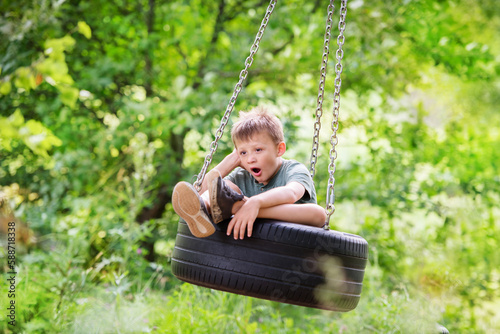 sad and boring boy yawning in a swing tire in the forest. Quarrel with friends, resentment, loneliness, boredom, yearning © Yulia