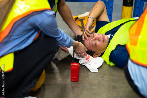 First Aid. Engineering supervisor helping to give first aid to head injured foreman lying unconscious at industrial factory. Professional engineering teamwork concept.