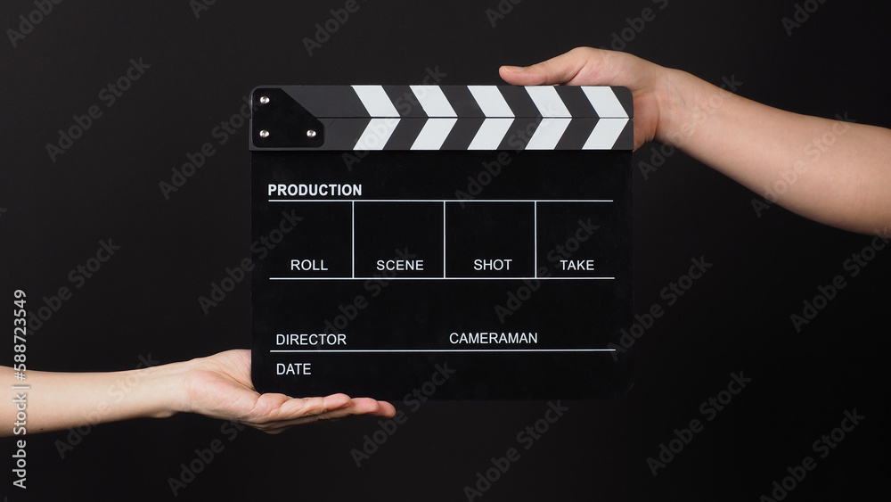 Two hands send and hold Black clapper board or movie slate on black background.