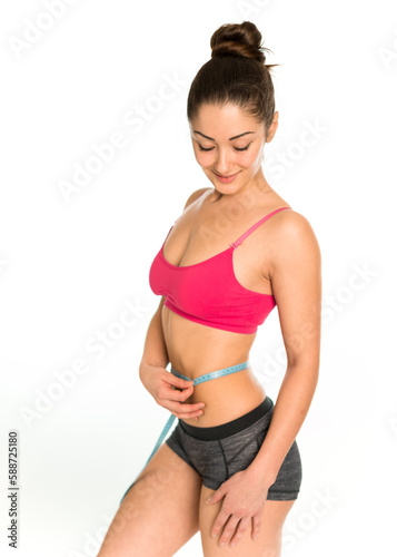 Pretty fit asian smiling woman in sport wear measure waist. Flat stomach with measuring tape. Measuring a woman's waist with a measuring tape. Concept of sport, healthy diet, fitness lifestyle.