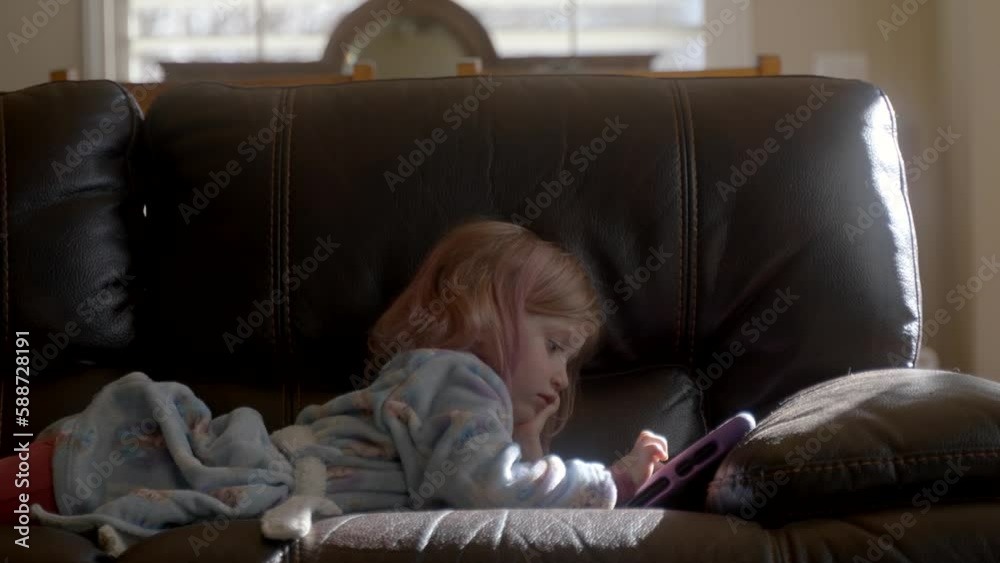 Per-school girl on the couch playing an educational game on a tablet Per-school girl on the couch playing an educational game on a tablet