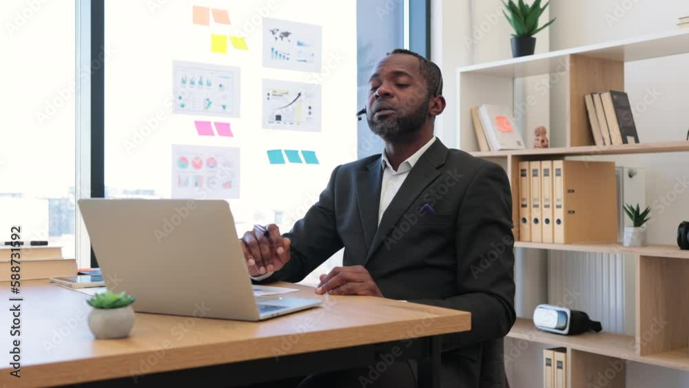 African american man in formal suit having video call at office using headset and wireless laptop. Transparent board with various graphs and charts on background. Concept of online business meeting. African american man in formal suit having video call at office using headset and wireless laptop. Transparent board with various graphs and charts on background. Concept of online business meeting.
