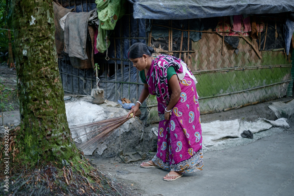 South asian rural housewife sweeping house yard with a broom wearing