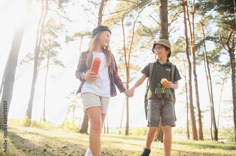 Obraz premium Happy excited school children with backpacks in casual clothes enjoying walk in forest on sunny autumn day, two active kids boy and girl running and playing together during camping trip in nature.