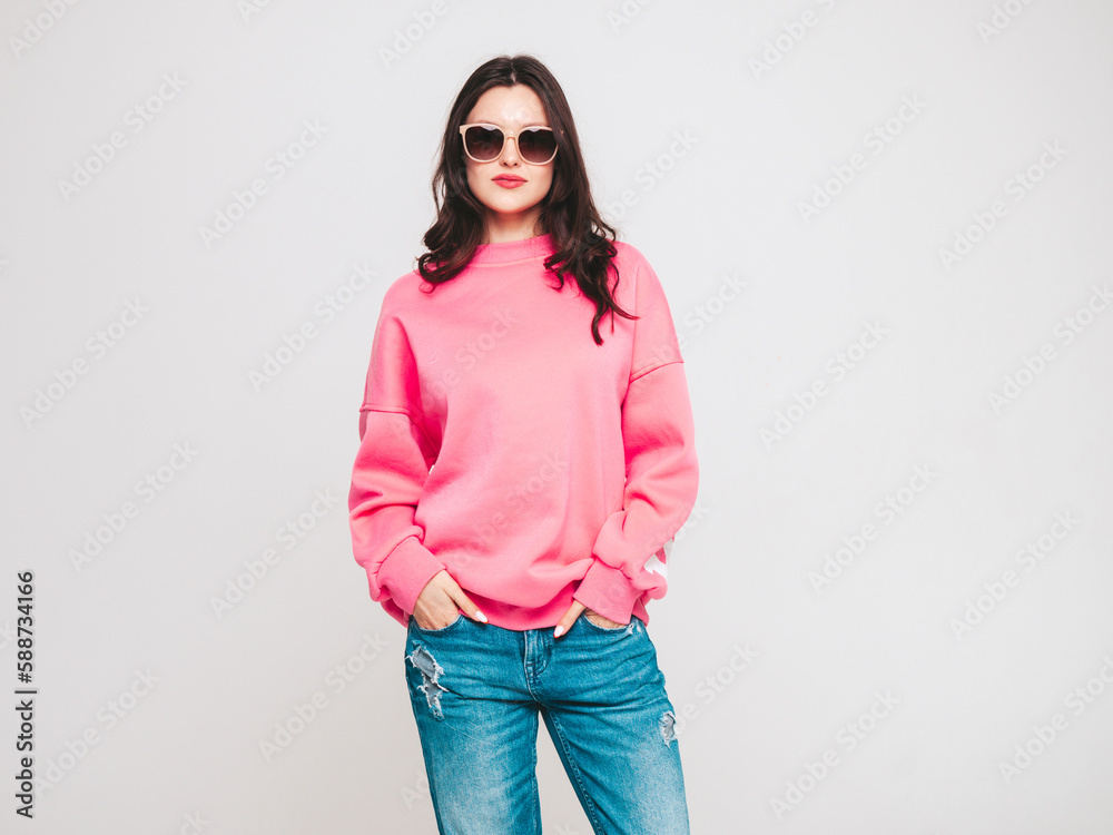 Young beautiful smiling female in trendy summer jeans and pink sweater clothes. Sexy carefree woman isolated on white wall in studio. Positive model having fun. Cheerful and happy. In sunglasses Young beautiful smiling female in trendy summer jeans and pink sweater clothes. Sexy carefree woman isolated on white wall in studio. Positive model having fun. Cheerful and happy. In sunglasses