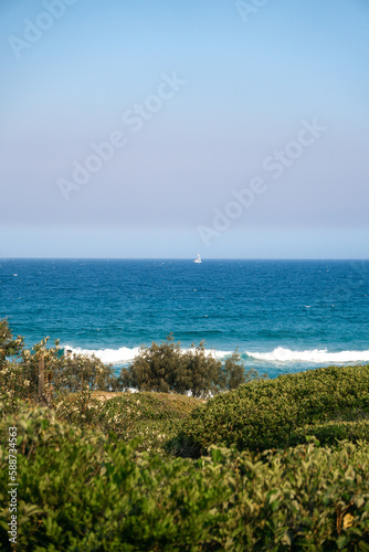 Beautiful romantic view of the white sailboat in the ocean visible from the path on the hill leading to the beach. 