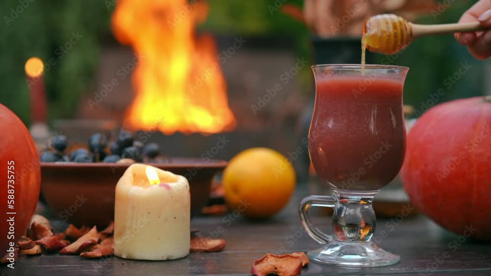 Close-up mixing smoothie with honey outdoors and burning fire at background. Female Caucasian hand adding sweet dessert preparing healthful drink on the right Close-up mixing smoothie with honey outdoors and burning fire at background. Female Caucasian hand adding sweet dessert preparing healthful drink on the right
