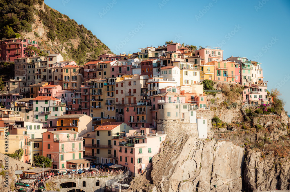 Manarola, a coastal town in Italy, showcasing the colorful houses that line the steep hillsides overlooking the sea, with a small harbor and boats in the foreground, and the blue waters 