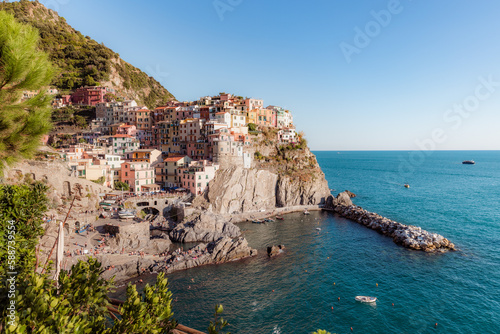 Manarola, a coastal town in Italy, showcasing the colorful houses that line the steep hillsides overlooking the sea, with a small harbor and boats in the foreground, and the blue waters 