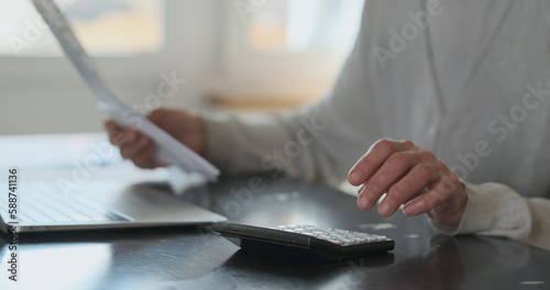 Elderly Woman's hands hold bills for services and calculate cost figures on calculator. Close-up, side view. Concept of financial literacy