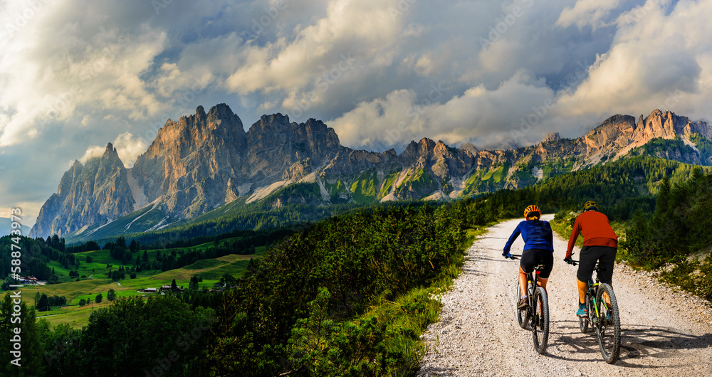A man and woman ride electric mountain bikes in the Dolomites in Italy. Mountain biking adventure on beautiful mountain trails.