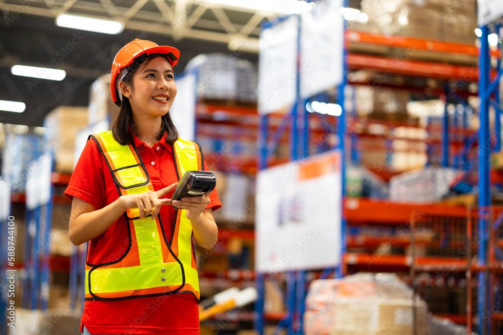 Warehouse female staff worker wearing hardhat helmet working on barcode scanner handheld at warehouse factory Warehouse female staff worker wearing hardhat helmet working on barcode scanner handheld at warehouse factory