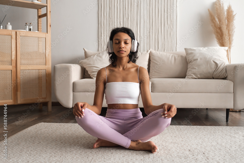 Front view on Young fit healthy African American woman in sportswear sitting at home doing yoga, meditating and breathing in the morning. Mental health and wellbeing banner with place for text Front view on Young fit healthy African American woman in sportswear sitting at home doing yoga, meditating and breathing in the morning. Mental health and wellbeing banner with place for text