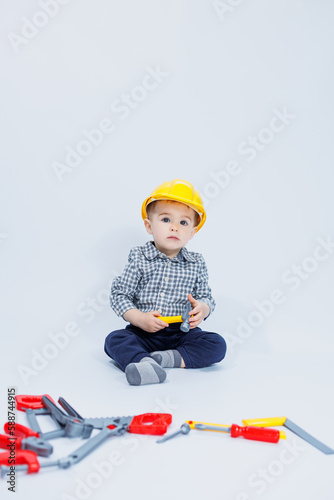 A little boy in a checkered shirt in the image of a builder. A boy in a construction helmet and plastic tools