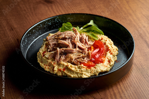 Hummus with chicken and pita in a black plate. Wooden background