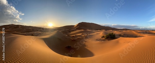 Dunes in the Sahara desert, Merzouga desert, grains of sand forming small waves on the dunes, panoramic view. Setting sun. Morocco. Reflections of the sun on the objective lens