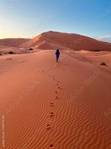 Dunes in the Sahara desert, Merzouga desert, grains of sand forming small waves on the dunes, panoramic view. Setting sun. Morocco. Girl that walk on a sand dune. Shoe prints